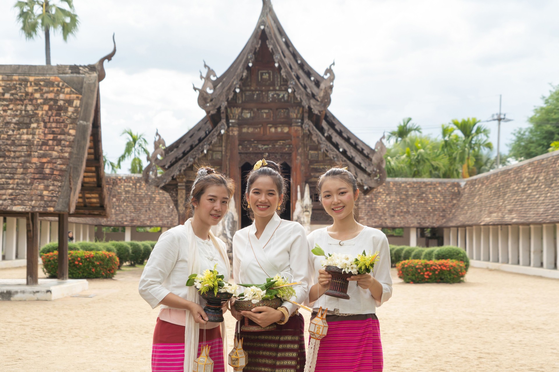 Portrait of group of Asian Shan women girls, Tai Yai, northern Thai people with traditional Lanna clothes holding flowers at Wat Ton Kwen temple, lanterns decoration. Culture lifestyle.