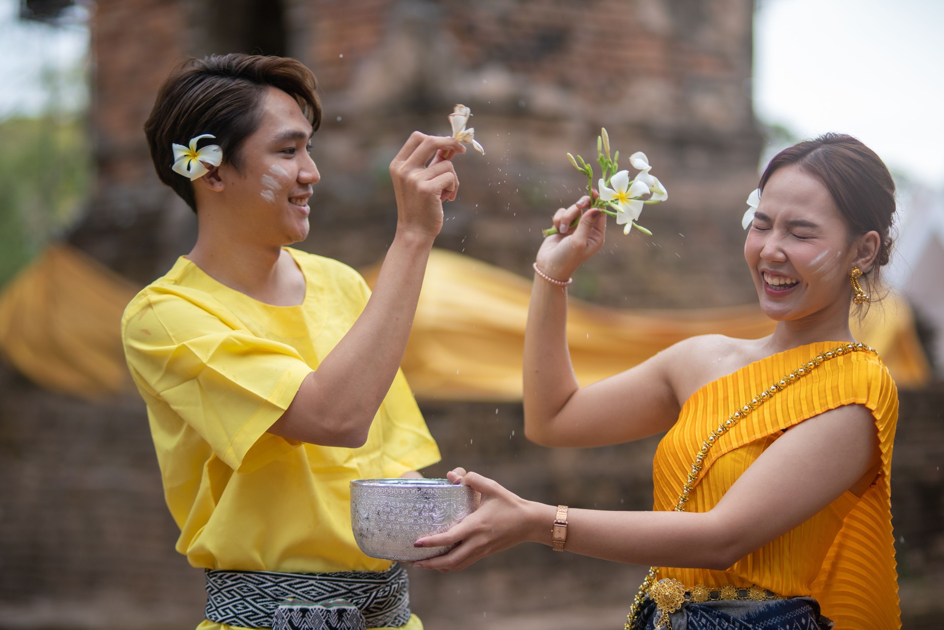 A beautiful Young Thai couple wearing Thai costumes playing in the water during Songkran in the temple